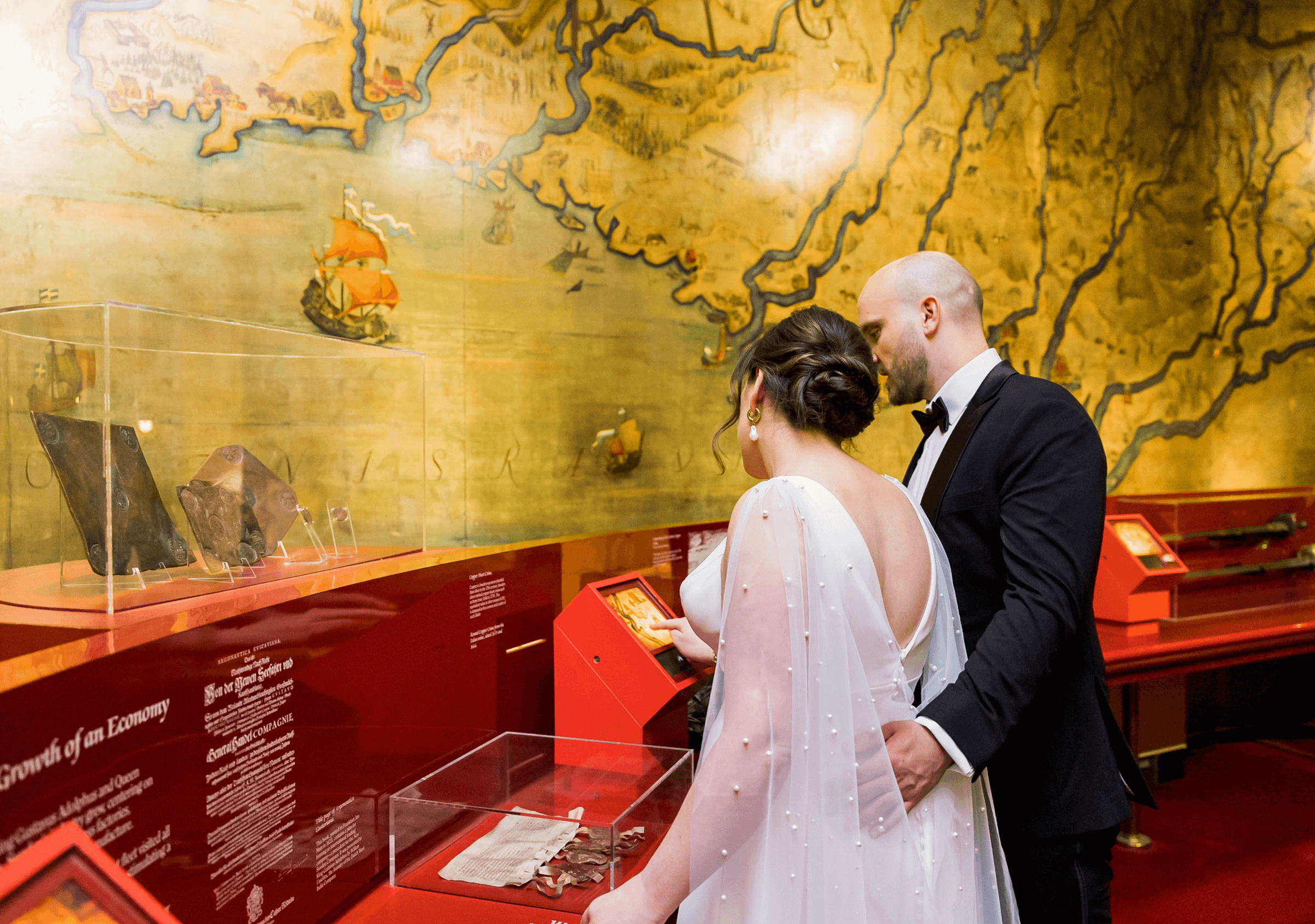 A couple examines museum exhibits in a room with a large vintage map on the wall. The glass cases display various historical artifacts.