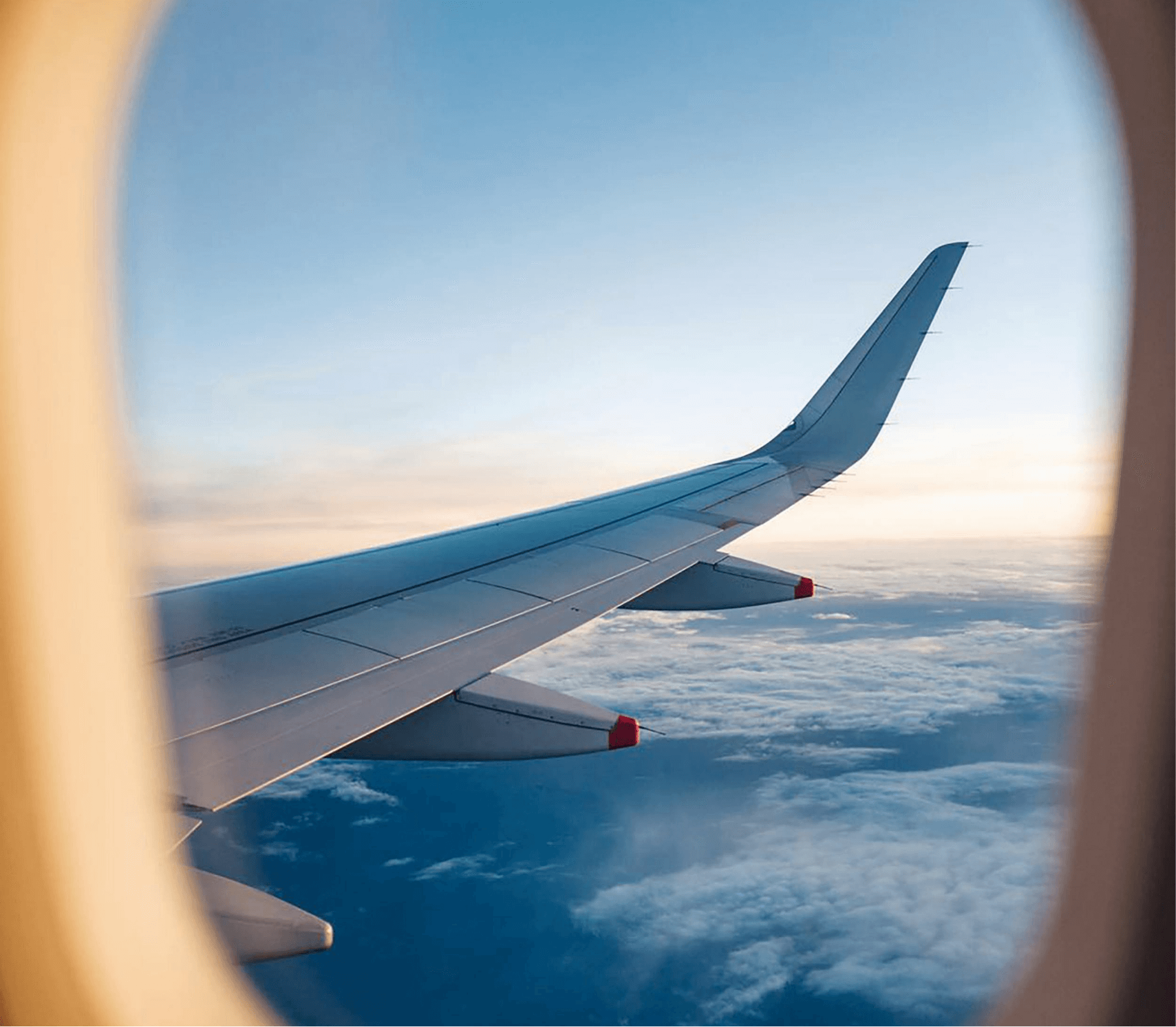 View from an airplane window showing the wing against a backdrop of clouds and a blue sky.