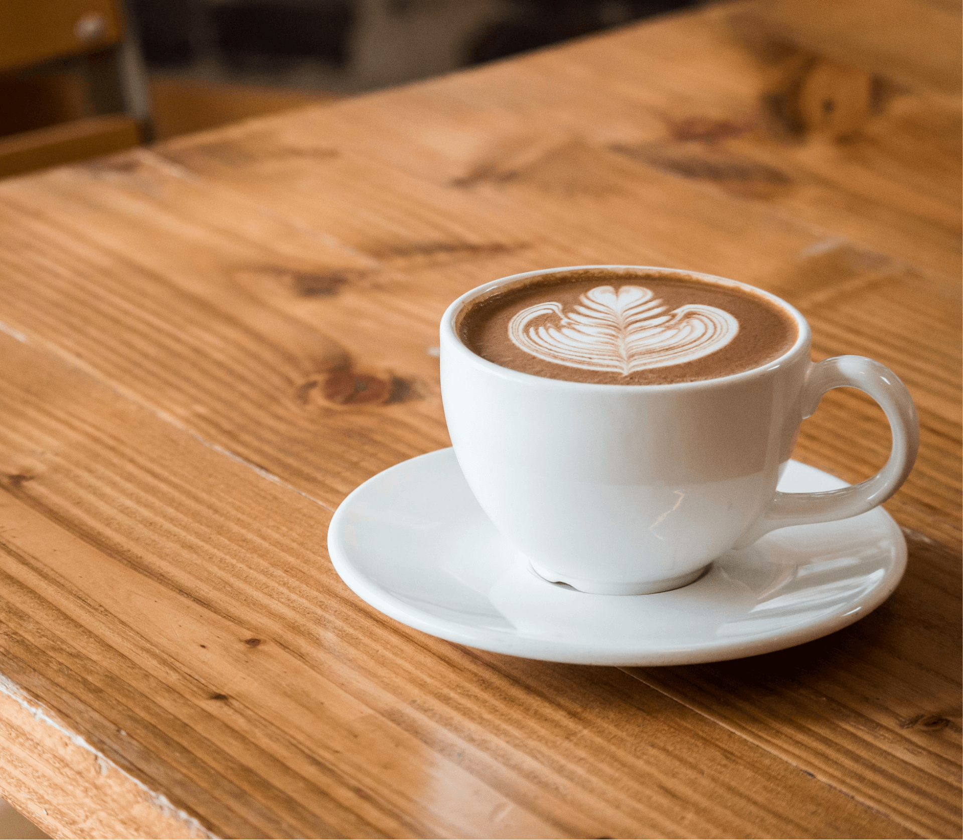 A cup of latte with heart-shaped latte art on a white saucer, placed on a wooden table.