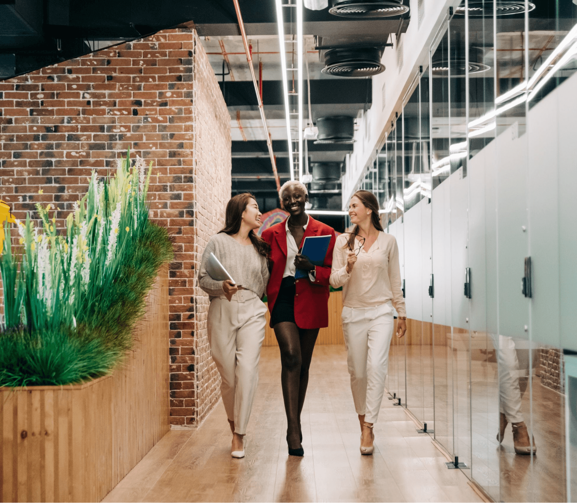 Three people walk down an office hallway, smiling and talking, while holding documents.