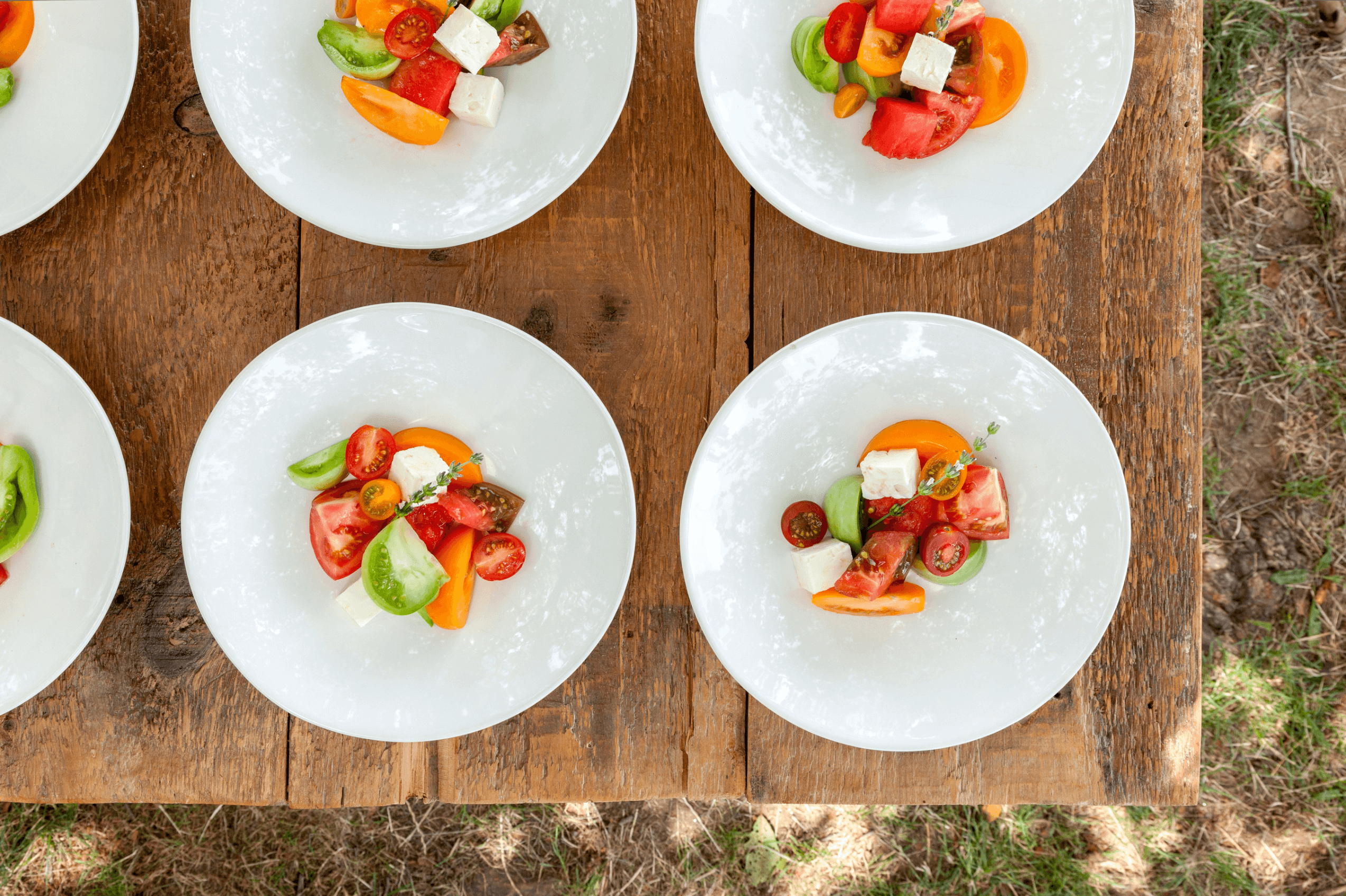 Several plates on a wooden table, each displaying a colorful salad with tomatoes, cucumbers, and cheese, viewed from above.