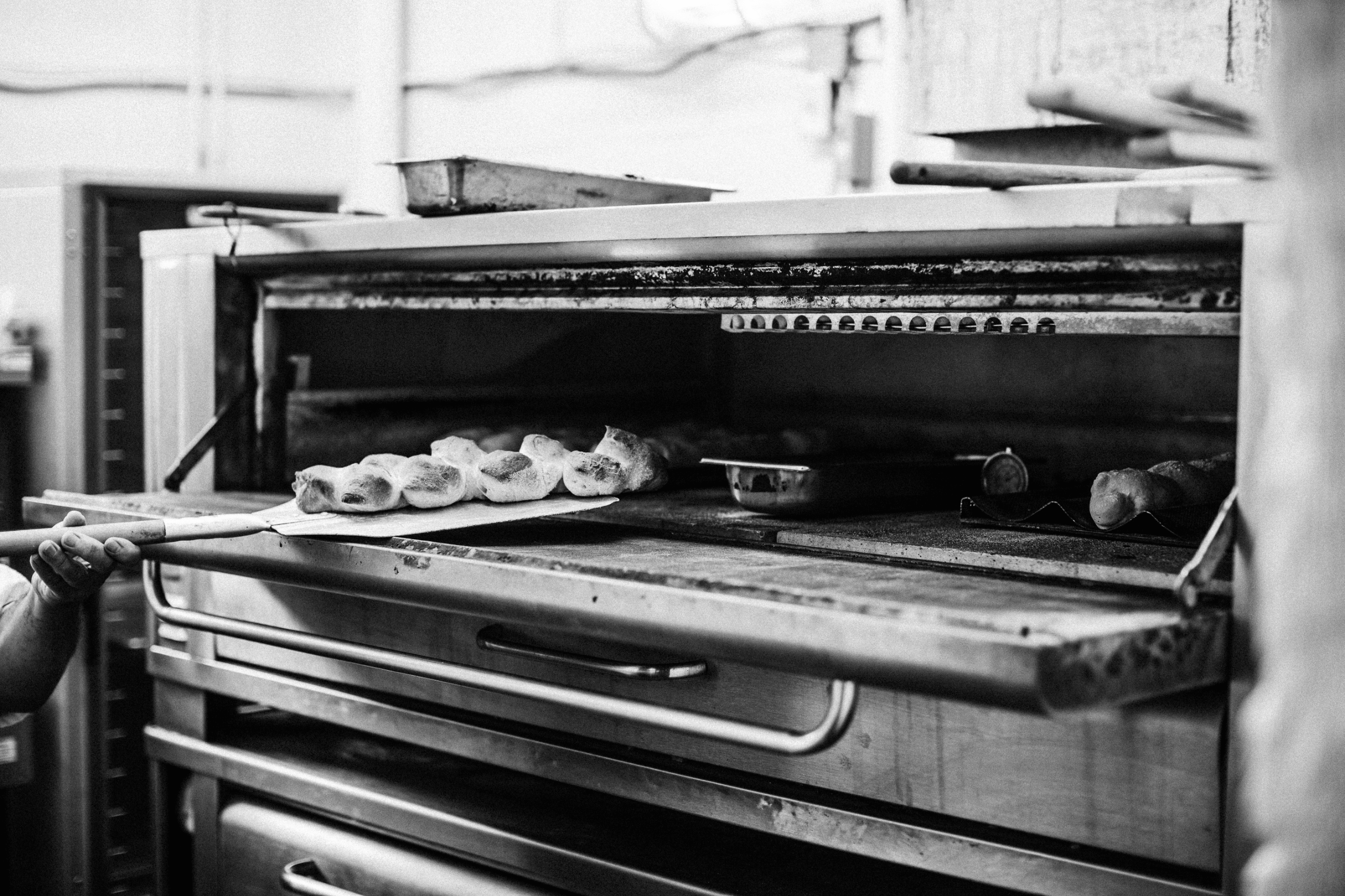 Bread loaves being placed into an industrial oven with a paddle in a bakery setting.