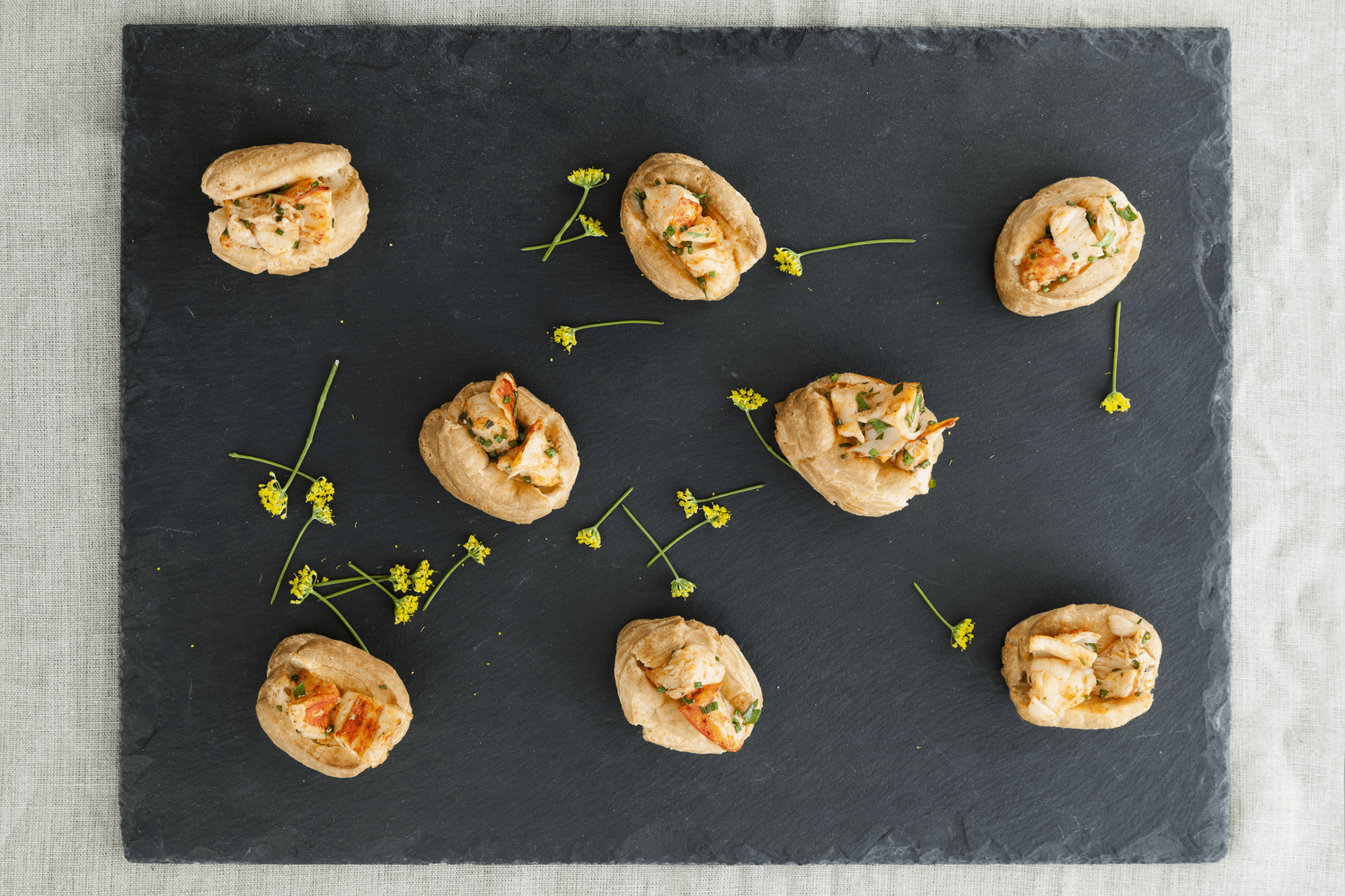 Eight stuffed pastries with herbs on a black slate surface, garnished with small green sprigs.