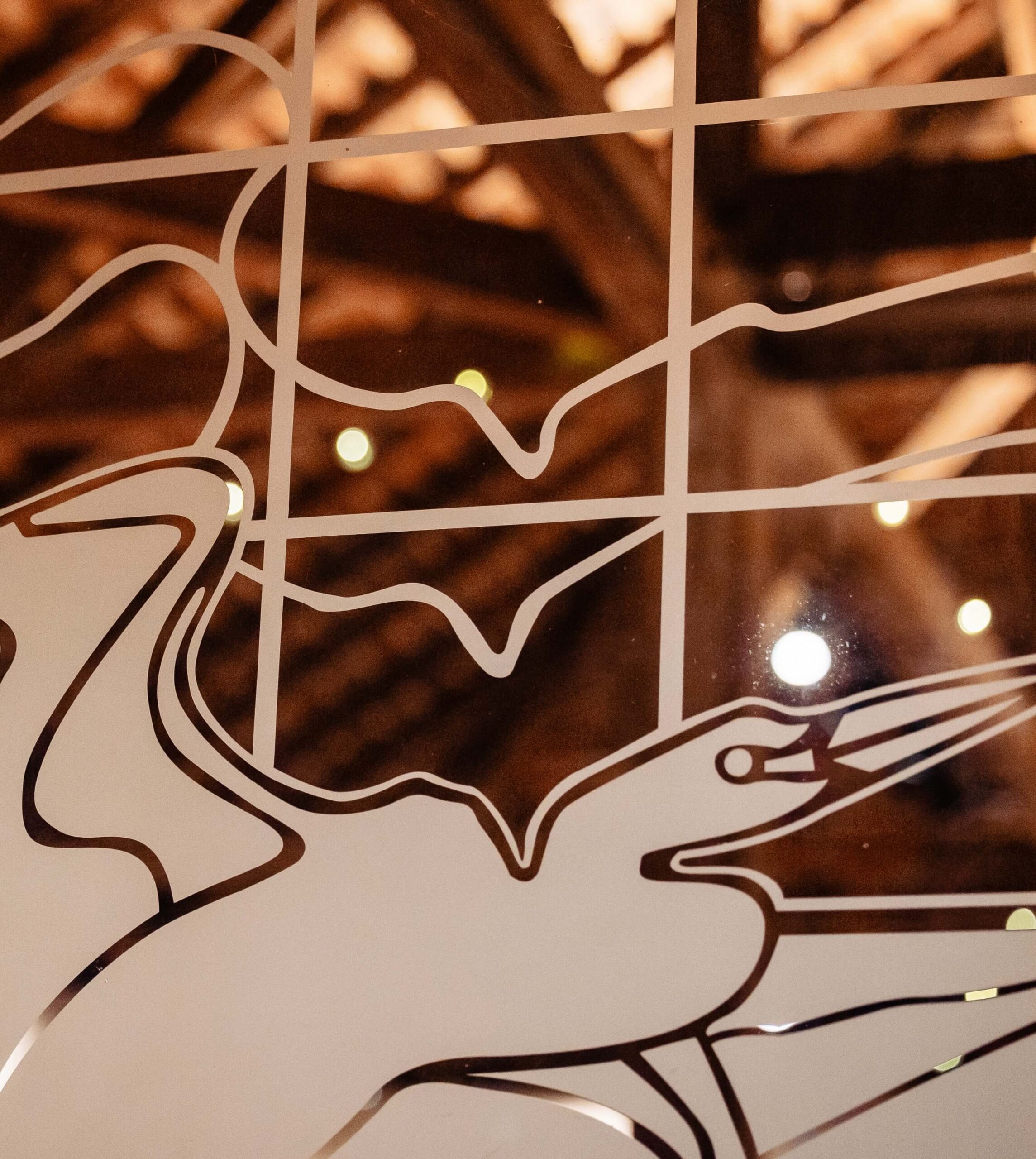 Abstract line art on glass with a criss-cross pattern in the background, and a softly lit ceiling visible through the glass.