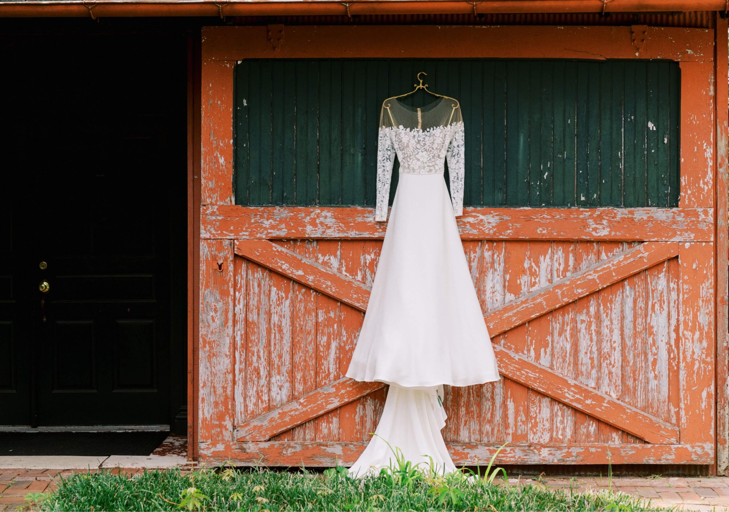 A long-sleeved white wedding dress hangs on a red and green rustic wooden door.