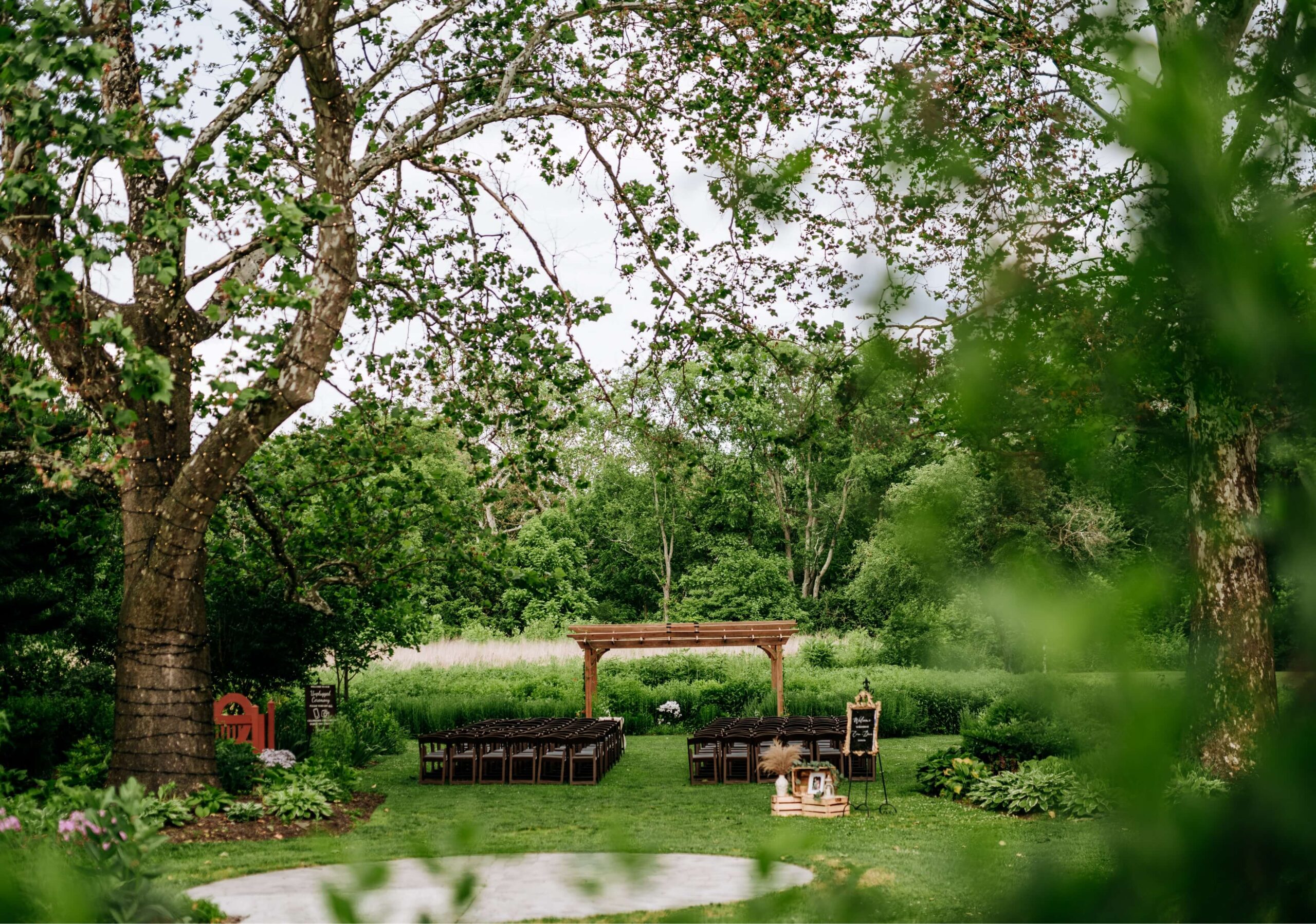 Outdoor wedding ceremony setup with wooden arbor, rows of chairs, and greenery in the background.