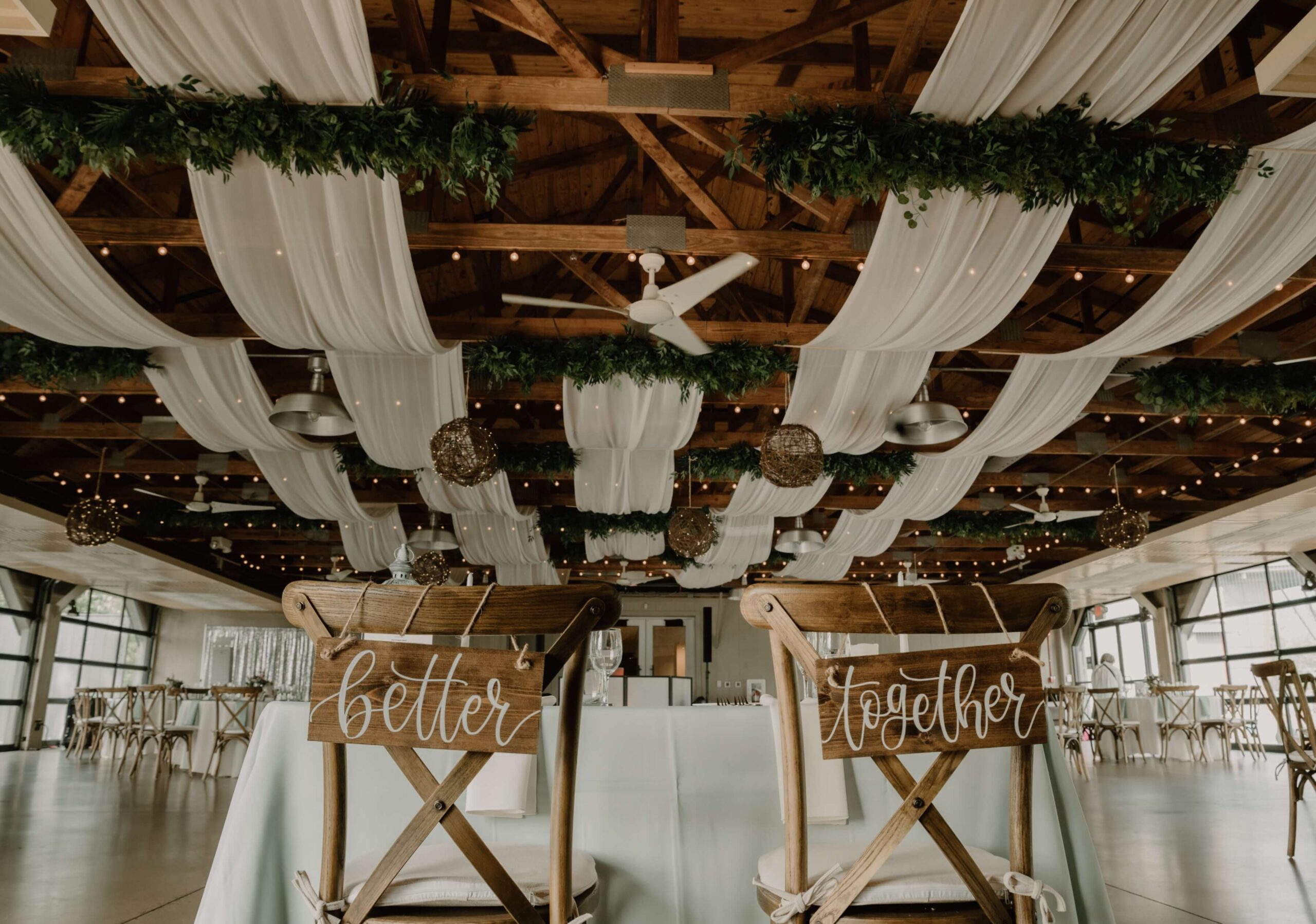 Wedding venue with draped fabric and string lights on ceiling. Two chairs with signs saying 
