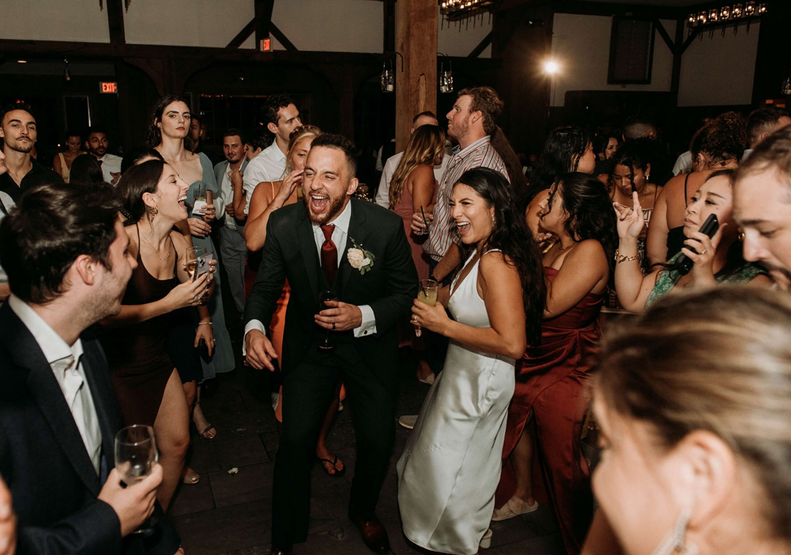 A group of people in formal attire dance and laugh at a lively indoor event.