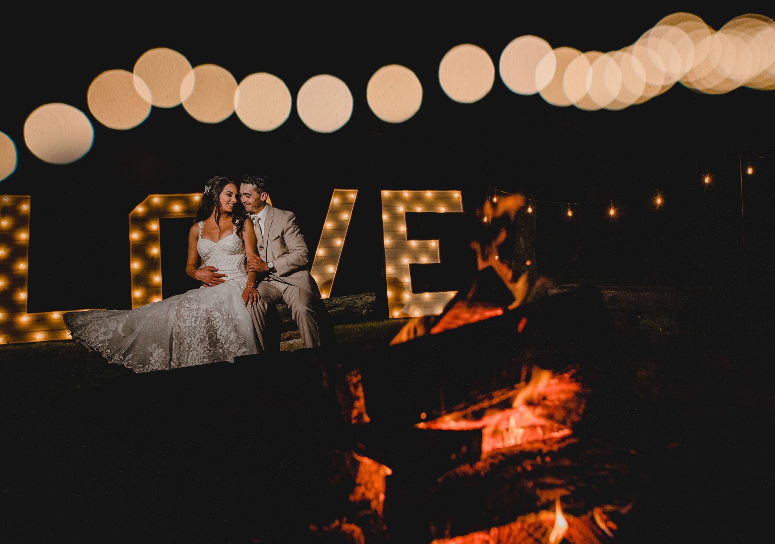 A couple sits together in wedding attire, illuminated by a large 