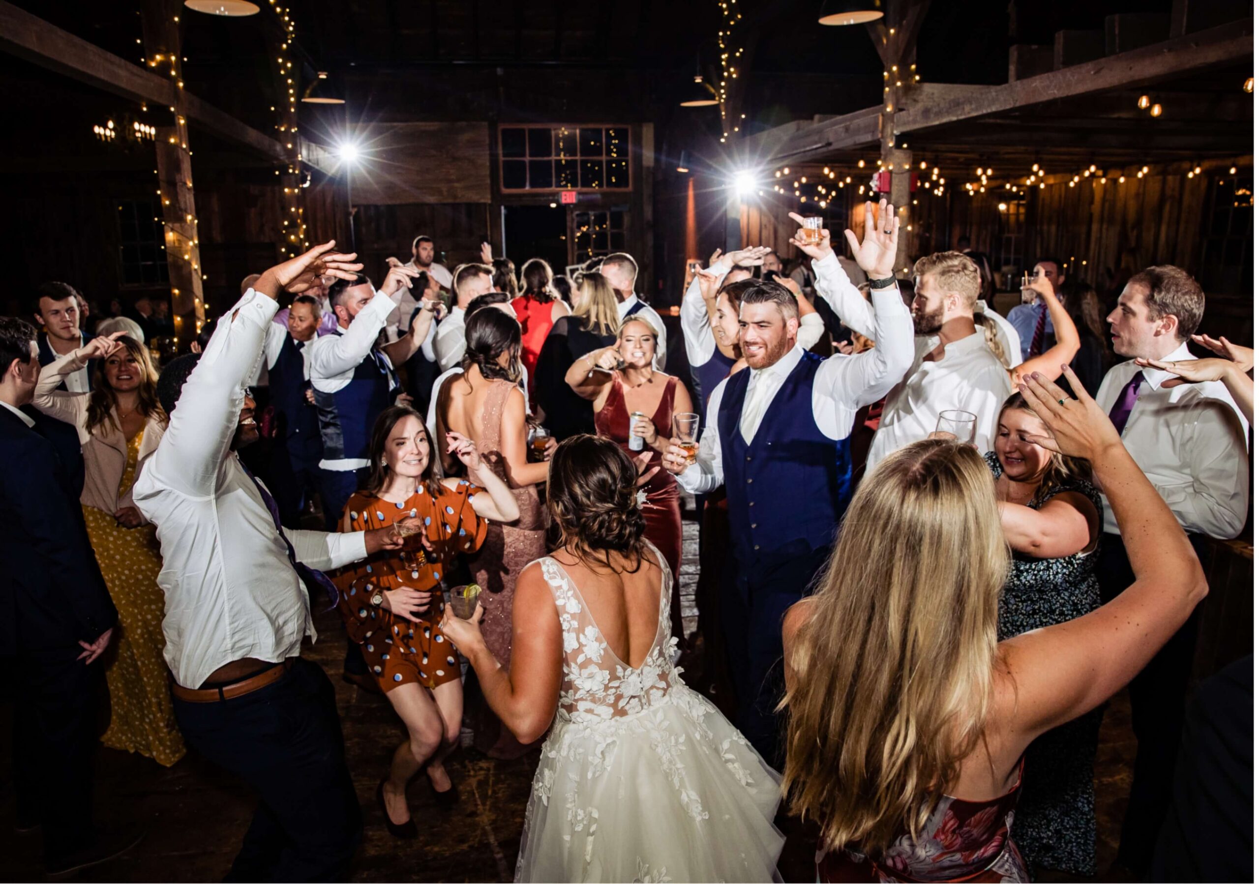 People dance energetically at a lively indoor event, surrounded by twinkling lights and wearing formal attire.