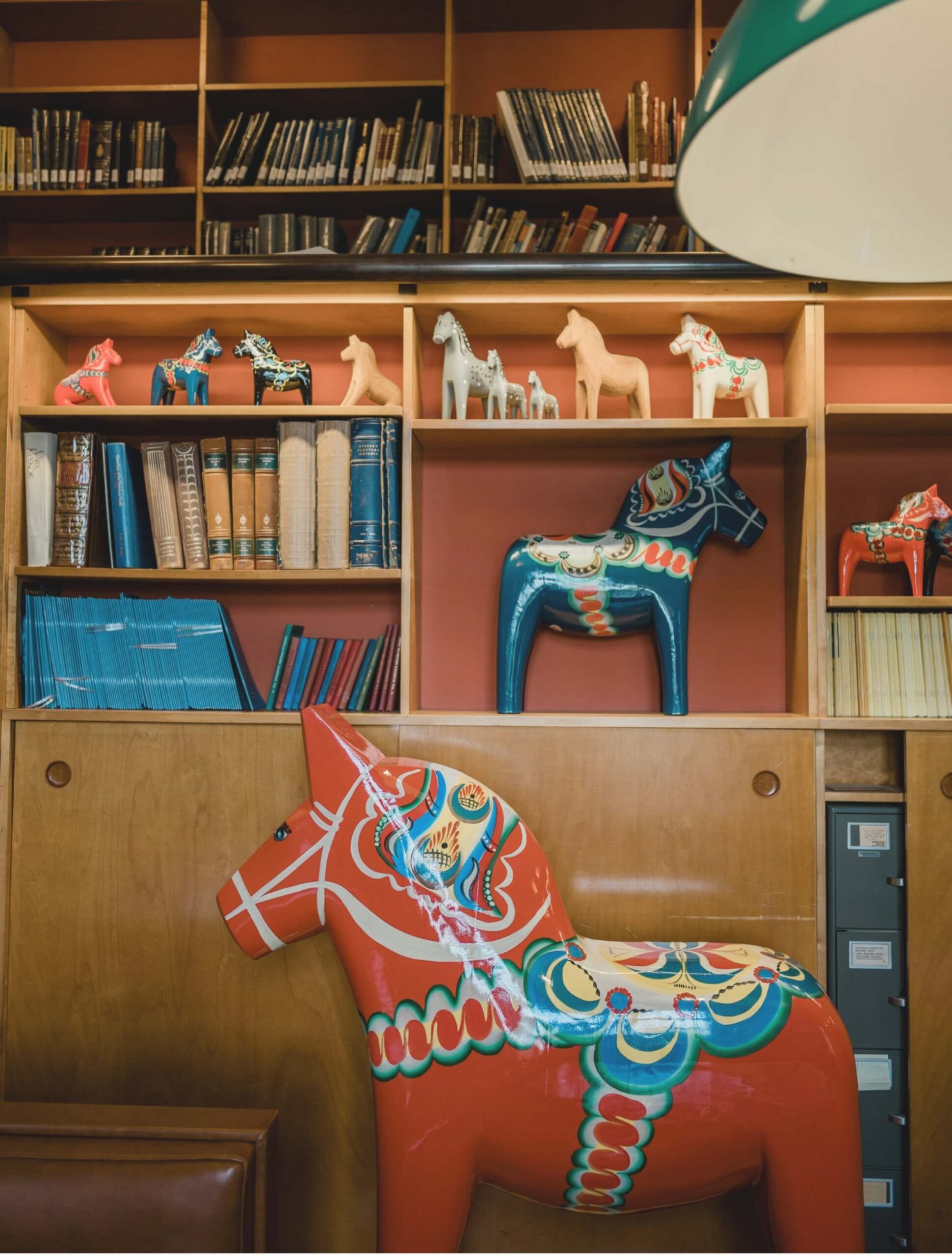 Shelves filled with books and colorful, decorative horse figurines in varying sizes. A large red patterned horse stands in the foreground.