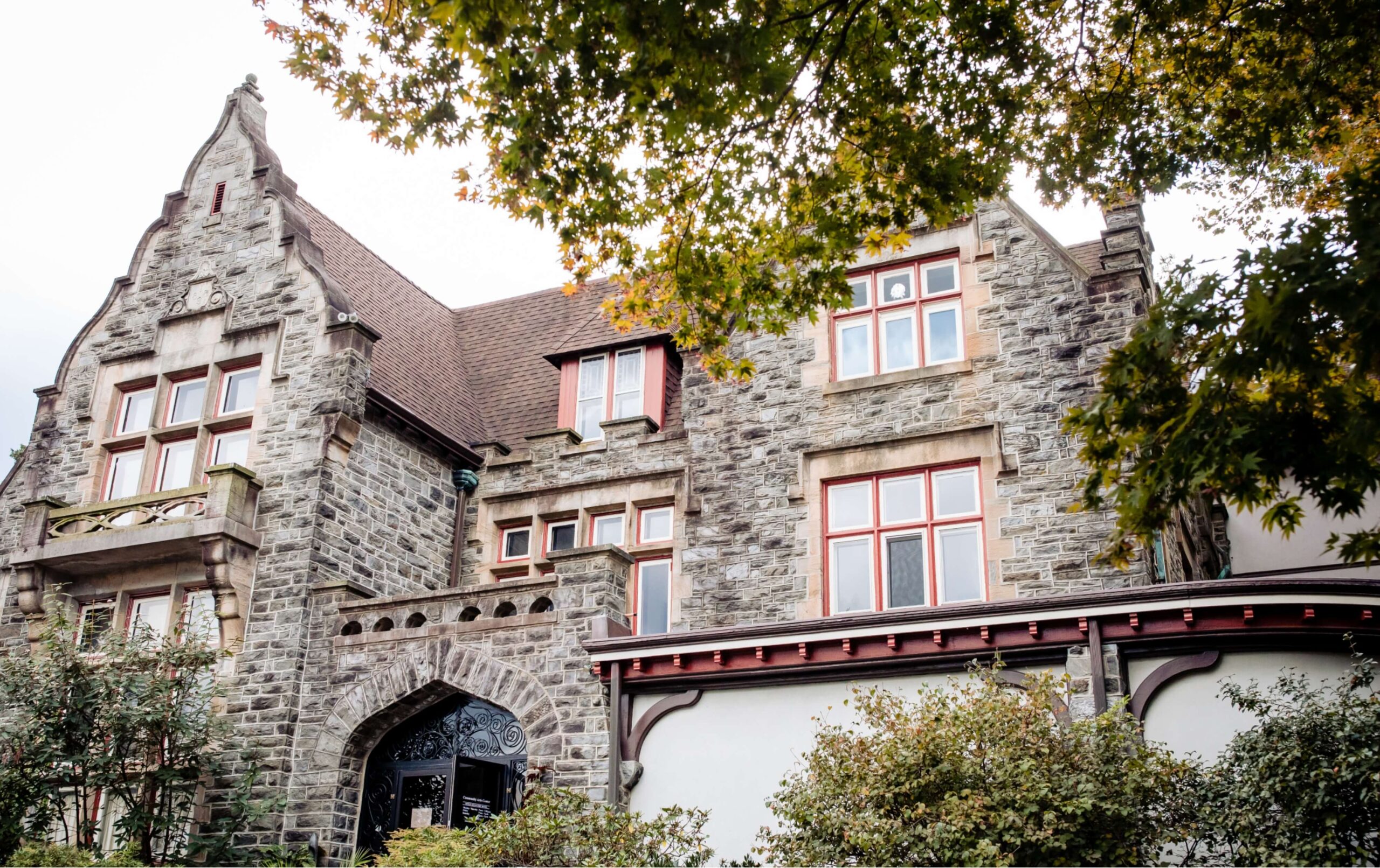 A historic building with a stone facade, pointed gables, and arched windows, surrounded by leafy trees.