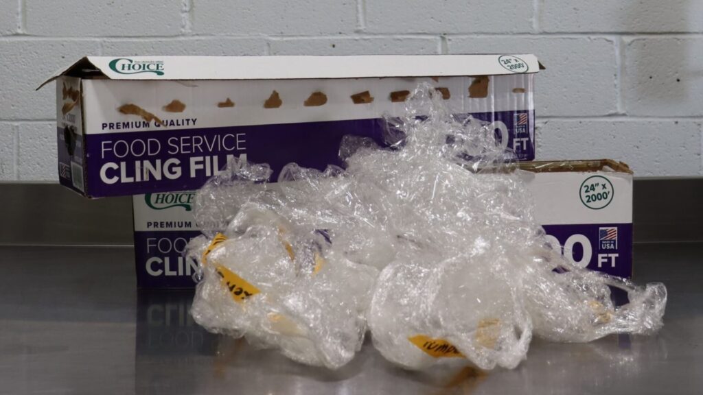 Two opened boxes of Choice brand food service cling film with used plastic wrap scattered in front, on a stainless steel surface.