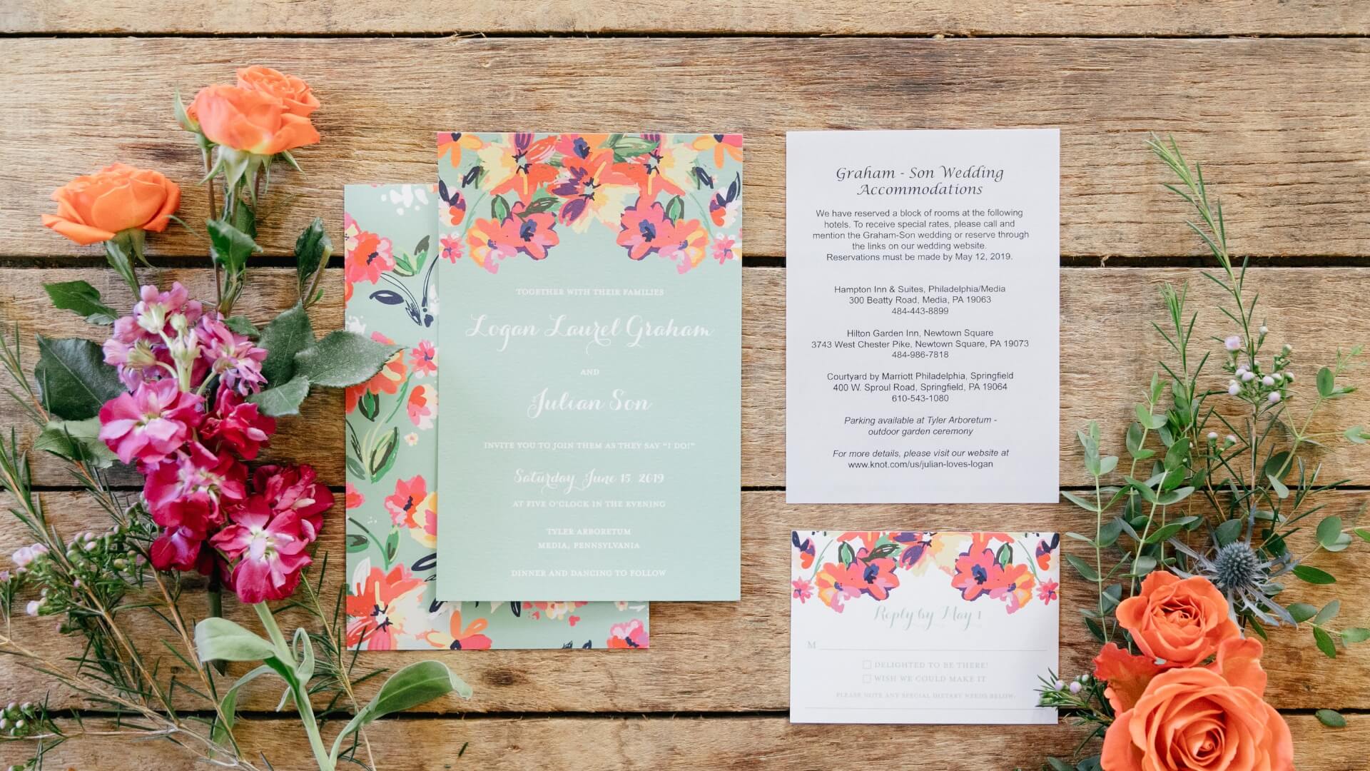 Floral-themed wedding invitation suite on a wooden surface, accompanied by bright pink and orange flowers.