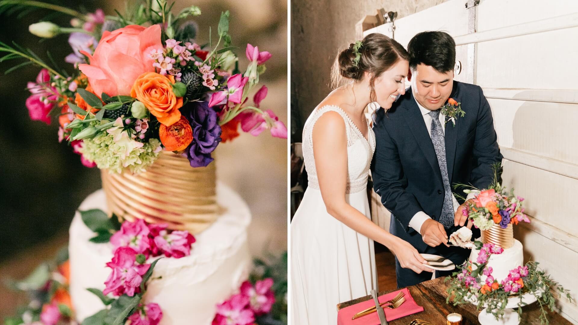 A couple cuts a white cake adorned with vibrant flowers, including pink, orange, and purple blooms, set against a rustic background.