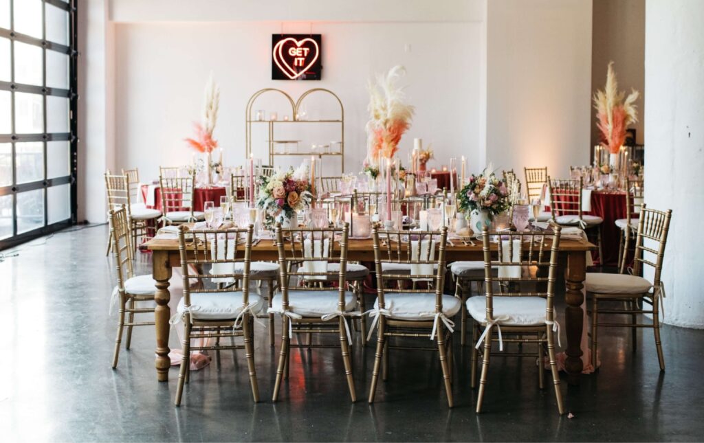 Elegant banquet table with gold chairs and floral centerpieces in a bright room, featuring a neon 